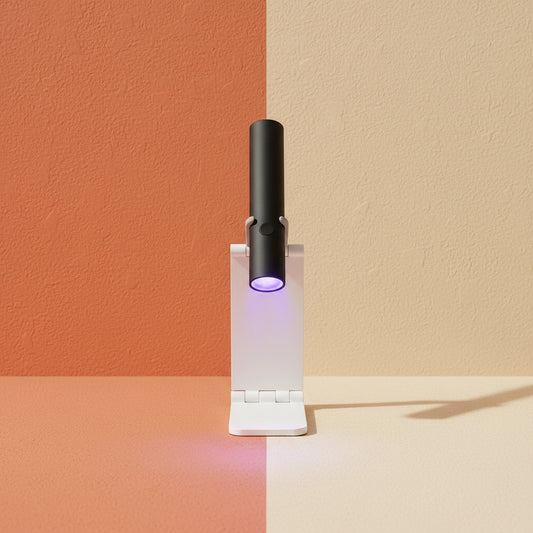 A lifestyle image of the Shazory mini cordless UV/LED nail lamp in black, mounted on its white foldable stand. It is being used to flash cure purple gel nail art on a desk with a passport and accessories, available at getshazory.com